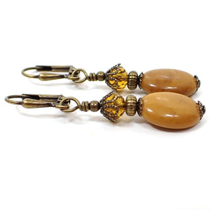 Side view of the handmade gemstone earrings. The metal is antiqued brass in color. There are faceted glass crystal beads at the top in a citrine orange color. The bottom jasper beads are oval shaped and have shades of mustard yellow, brown, and hints of orange.