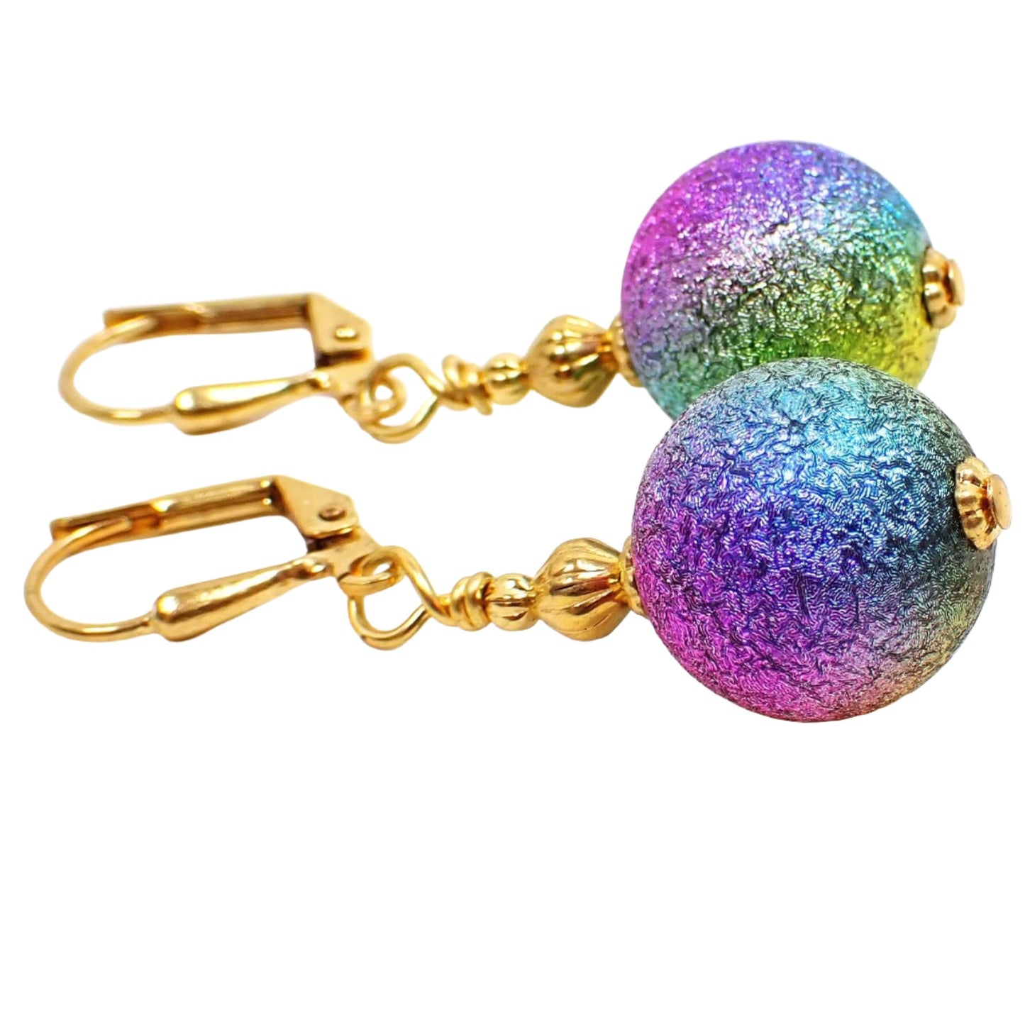 Side view of the handmade metallic rainbow earrings. The metal is gold plated in color. There are large round ball beads at the bottom that are textured and have metallic colors of the rainbow blended all the way around the beads.