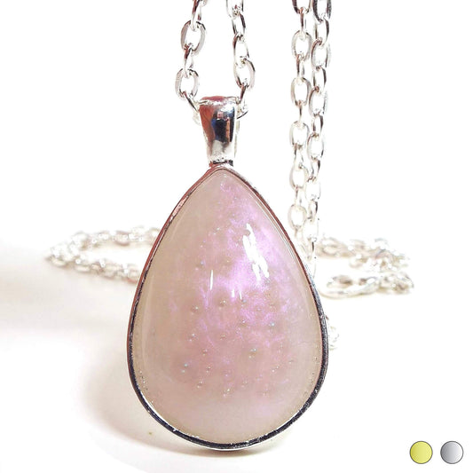 Front view of the handmade teardrop bubble resin necklace. The teardrop resin cab has pearly color shift resin with a light light pink and off white colors. Inside the resin are tiny AB clear bubbles. The bottom corner shows two color swatches for a choice of gold tone or silver tone plated setting. 