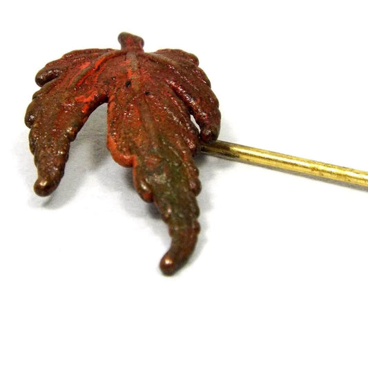 Magnified view of the top part of the Mid Century vintage leaf stick pin. the leaf is enameled in brown, orange, and green tones. The metal is gold tone in color.