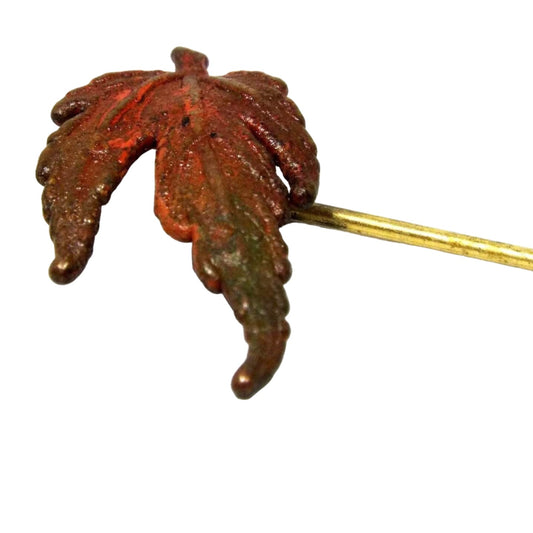 Magnified view of the top part of the Mid Century vintage leaf stick pin. the leaf is enameled in brown, orange, and green tones. The metal is gold tone in color.