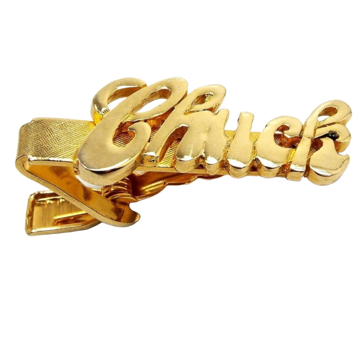 Angled front view of the retro vintage name tie clip. The metal is gold tone in color. The name is shiny and the background is textured. It has the name Chuck in script lettering. There is a small dark spot on the inside area by the K. 