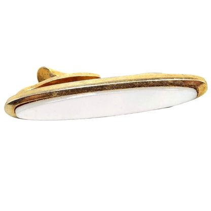Front view of the Mid Century vintage German tie clip. The metal is gold tone in color and it's shaped like a long oval. There is a pearly white mother of pearl shell cab in the middle.