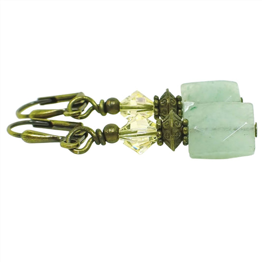 Angled view of the handmade green aventurine earrings. The metal is antiqued brass. There are faceted glass crystal beads in light yellow at the top. The bottom gemstone beads are faceted rectangles with shades of green.