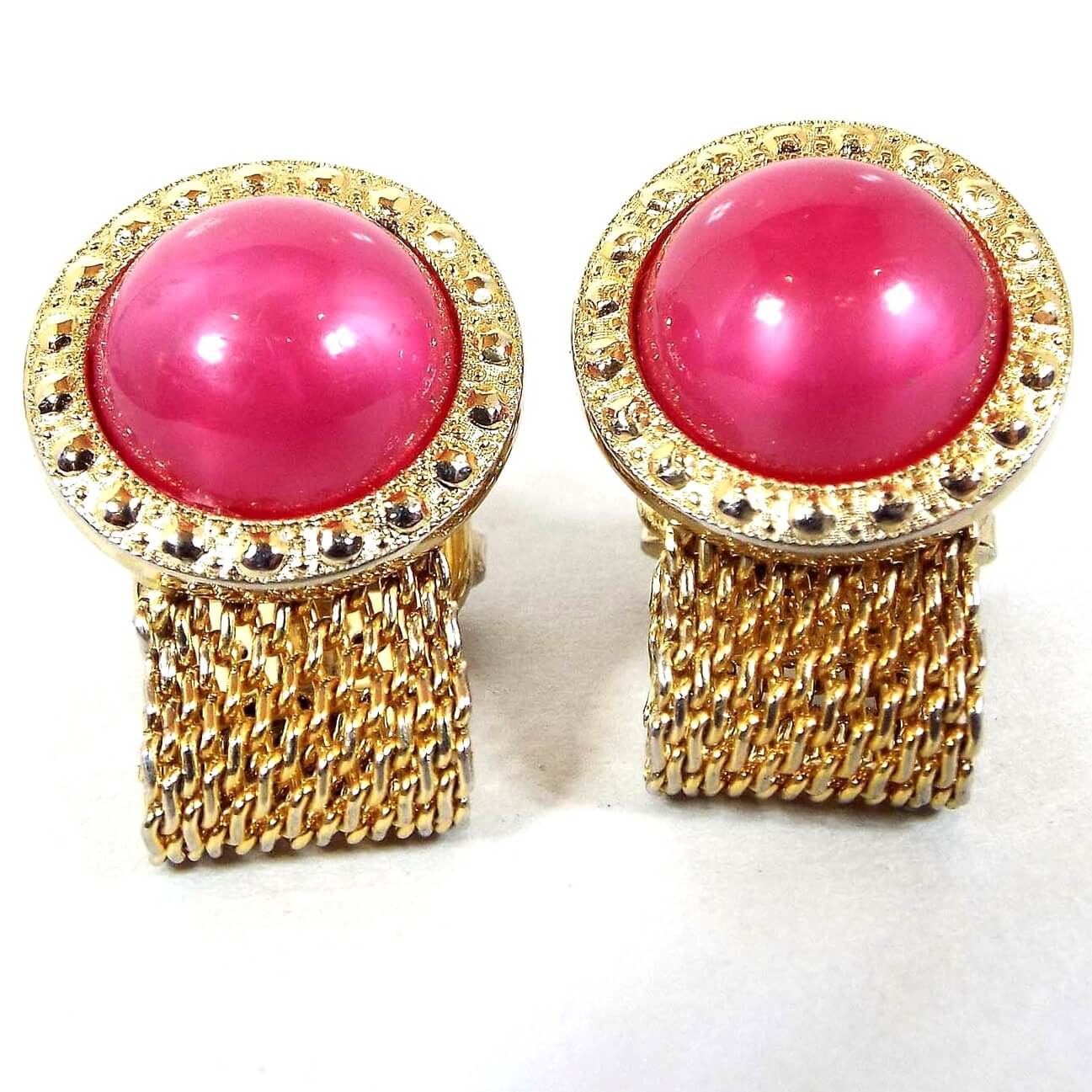Front view of the Mid Century vintage Foster mesh wrap around cufflinks. They are gold tone in color and have round tops with bright pink moonglow lucite cabs. The cabs are pearly pink and have a glowy effect as you move around.