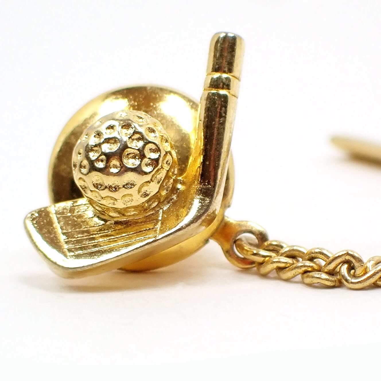 Front view of the retro vintage golfing tie tack. It is gold tone plated in color and has a golf club head and ball design. 
