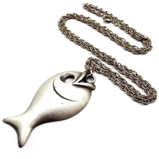 Front view of the pewter retro vintage fish pendant necklace. It has a darker silver tone color plated rope chain with a spring ring clasp at the end. The pendant is made of matte pewter in light gray color. It has a fish shape with large cut out eye area. 