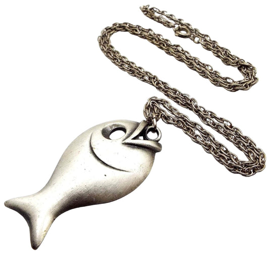Front view of the pewter retro vintage fish pendant necklace. It has a darker silver tone color plated rope chain with a spring ring clasp at the end. The pendant is made of matte pewter in light gray color. It has a fish shape with large cut out eye area. 