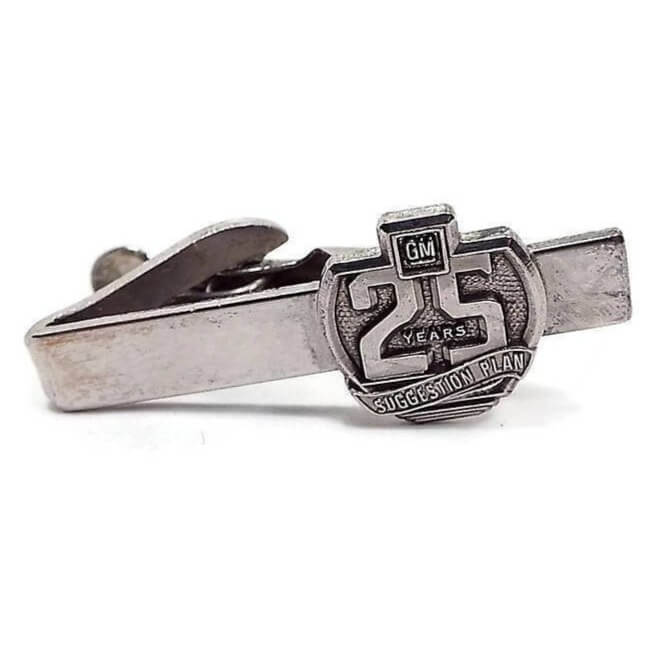 Front view of the Mid Century vintage GM tie clip. The metal is silver tone in color. It has the GM logo with 25 Years and Suggestion Plan on the front.
