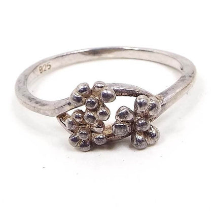 Front view of the retro vintage sterling silver flower ring. The silver is slightly darkened from age. The top part of the ring has a split metal area with three small flowers made from the sterling. The petals are rounded and puffy style. 925 is marked on the inside band. 