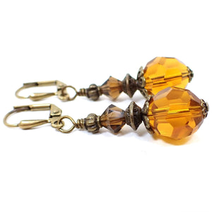 Side view of the handmade drop earrings with faceted glass crystals. The metal is antiqued brass in color. The top beads are brown and the bottom beads are a citrine orange color.