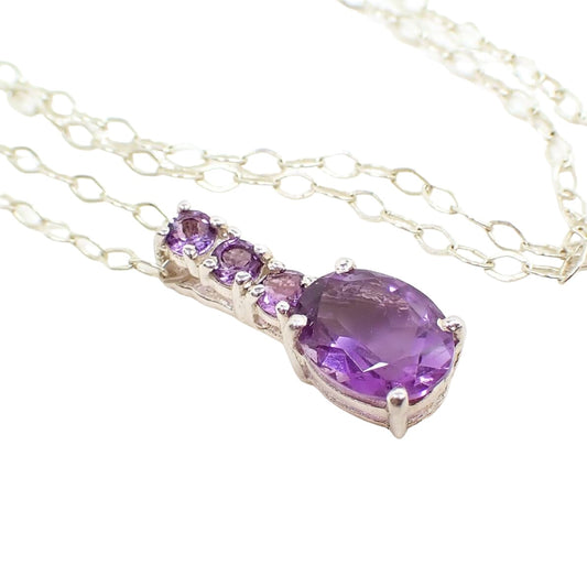 Enlarged front view of the pendant on the retro vintage gemstone pendant necklace. The chain and setting are sterling silver and bright silver in color. The pendant has three small round purple amethyst stones and a larger oval amethyst stone at the bottom. 
