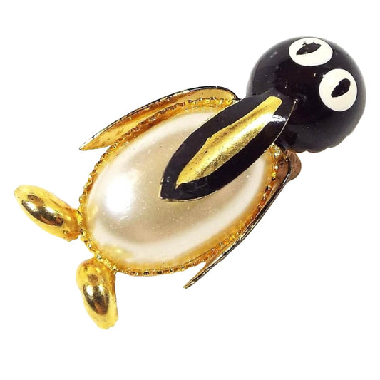 Front view of the Mid Century vintage penguin brooch pin. It has metal gold tone color and black enameled face, beak, and wings. The eyes are enameled white. The penguin's belly is a domed plastic faux pearl cab. 