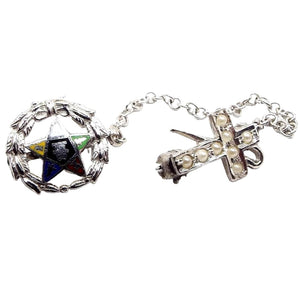 Enlarged front view of the Masonic Mid Century vintage scatter lapel pin set. The metal is silver tone in color. There are two tiny brooches connected by a short thin chain. The first one is a wreath with a multi colored enameled Masonic star in the middle. The second is a cross cane with tiny white faux pearls on the front. Part of the tiny safety clasp is showing on the cross cane pin.