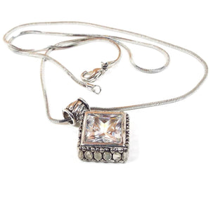 Angled front view of the 1990's retro vintage rhinestone pendant necklace. There is a silver tone snake chain with a lobster claw clasp. The pendant is diamond shape with a flashy clear rhinestone in the middle. 