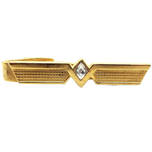 Front view of the retro vintage Speidel rhinestone tie clip. It is gold tone in color and has a modernist style design with flared ends and a waffle textured pattern. There is a diamond shaped clear glass crystal rhinestone in the middle.
