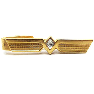 Front view of the retro vintage Speidel rhinestone tie clip. It is gold tone in color and has a modernist style design with flared ends and a waffle textured pattern. There is a diamond shaped clear glass crystal rhinestone in the middle.