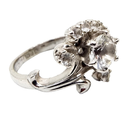 Angled front and side view of the Mid Century vintage sterling silver Quartz ring. The top part has a flower design with curved stem and leaves. There is a prong set round quartz gemstone in the middle of the flower and smaller sized prong set round quartz gemstones around the top of it. 