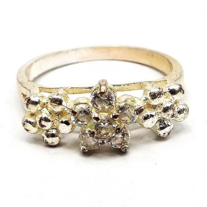 Front view of the retro vintage rhinestone floral ring. The metal is silver tone in color, but has a slight yellowing from age. There are three flowers on the top part of the ring over a split band. The middle flower has five prong set round clear rhinestones. The other two flowers are made of round metal balls and are on each side of the rhinestone flower.