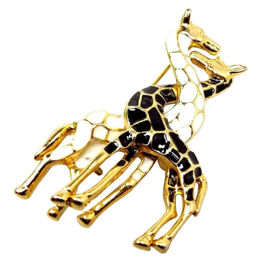 Front view of the retro vintage giraffe brooch. the metal is gold tone in color. There are two giraffes with their necks intertwined. One has white enameled spots and the other has black enameled spots.