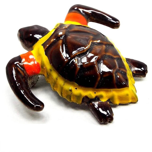 Front view of the Mid Century vintage enameled turtle brooch pin. The head, legs, and main part of the shell are dark brown in color. The edge of the shell is yellow and there are orange bands by the front legs. The head is jointed so it can move from side to side.