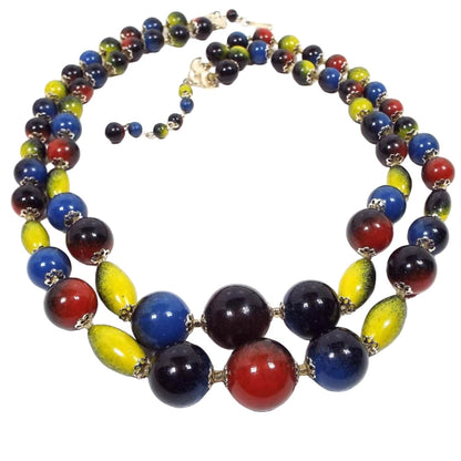 Top view of the multi color multi strand necklace from Japan. It has two strands of round and oval beads. The beads are black with sprayed on primary colors of red, blue, and yellow. There is a hook clasp at the end.