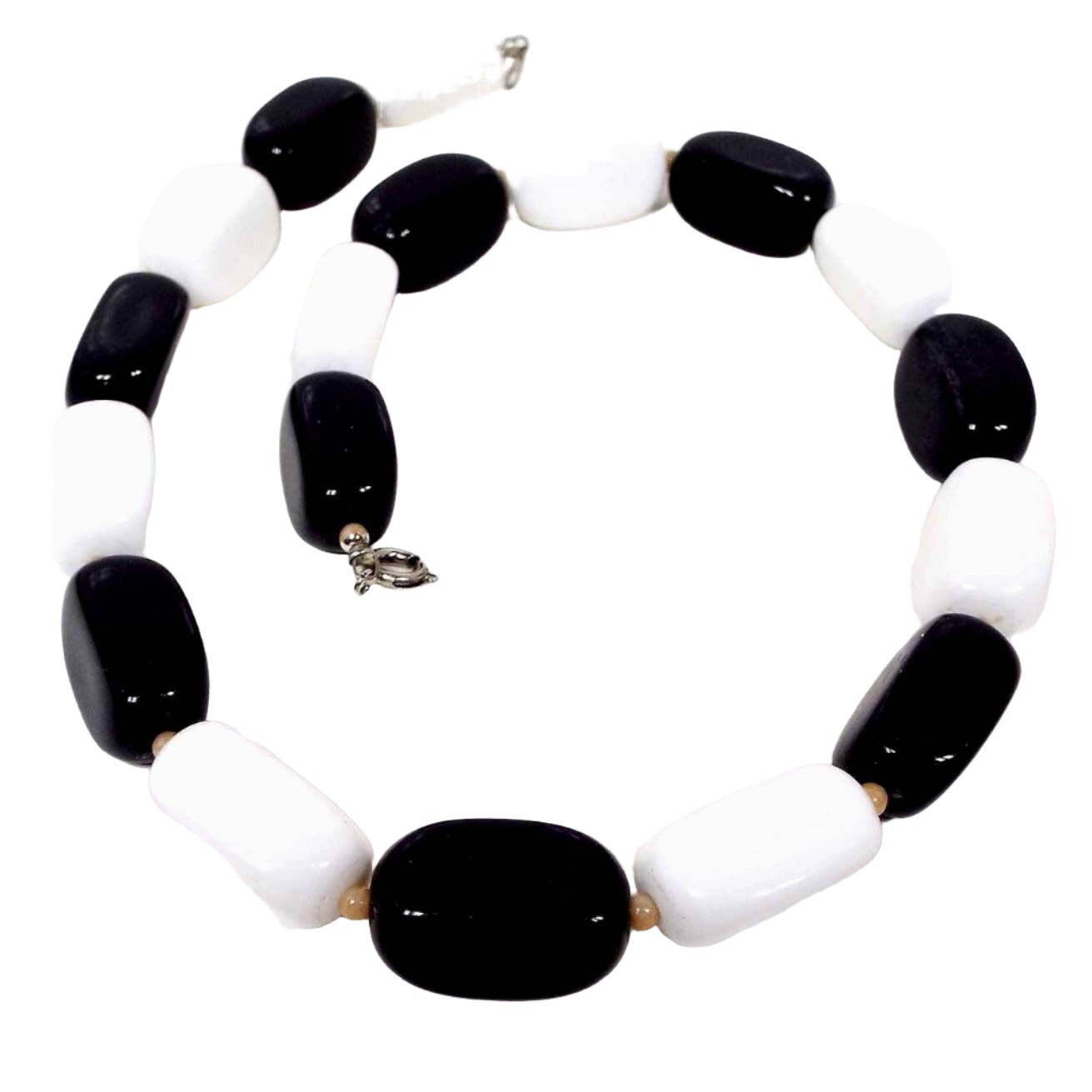 Front view of the retro vintage black and white lucite beaded necklace. The beads are rounded rectangle shape and alternate between black and white. There is a silver tone color spring ring clasp at the end and small light peach color seed beads in between the lucite beads.