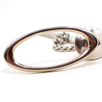 Enlarged front view of the retro vintage tie tack. It is shaped like a wide large open oval and is silver tone plated in color.