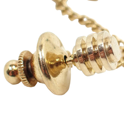 Enlarged front view of the retro vintage stud tie tack. The metal is gold tone plated in color. There are stacked flat circles with spaces in between going outward on the tie tack. 