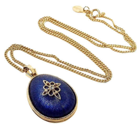 Front view of the retro vintage Avon pendant necklace. The metal is gold tone in color. The pendant is tear drop shaped with blue plastic cab and a rhinestone in the middle of a gold tone star shape. 