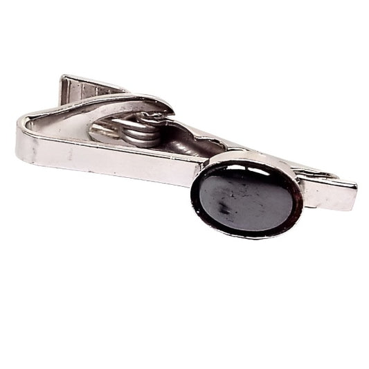 Front view of the retro vintage faux hematite tie clip. The metal is silver tone in color. There is an oval dark metallic gray glass cab on the end.