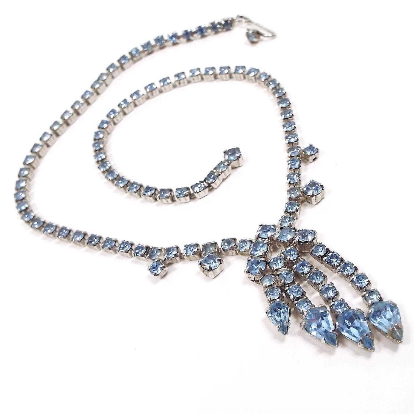 Front view of the Mid Century vintage blue rhinestone necklace. The cup chain is silver tone in color and has a hook clasp on the end. The bottom area has a chandelier style design with teardrop rhinestones on the end. The rhinestones are light blue in color.