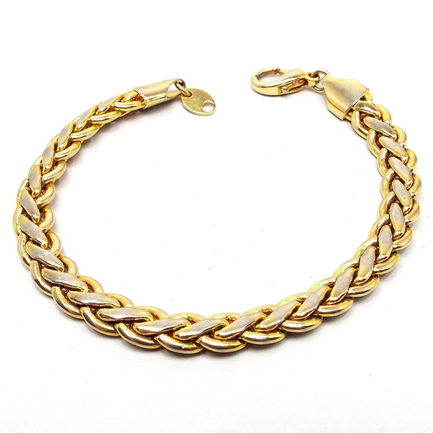 Top view of the retro vintage chain bracelet. It is gold tone in color with a lobster claw clasp. It has a braided woven design. There is some rub wear to the middle links where it is lighter in color when viewed closely.
