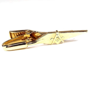 Front view of the retro vintage Masonic tie clip. It is gold tone in color and shaped like a trowel. It has a square, compass and G design in the middle. 