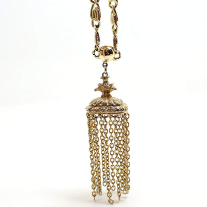 Enlarged front view of the pendant area on the Mid Century vintage chain tassel pendant necklace. The metal color is gold tone. The chain has large S links. The bottom pendant has a crest style top with a large oval that has strands of cable chain all the way around it. 