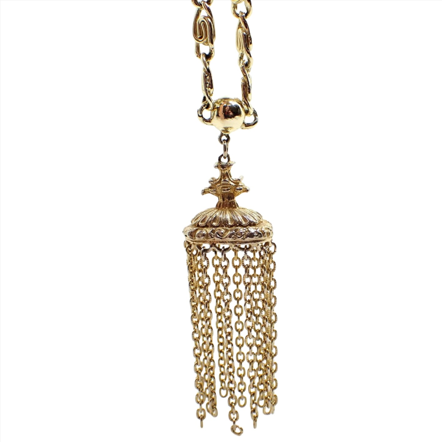 Enlarged front view of the pendant area on the Mid Century vintage chain tassel pendant necklace. The metal color is gold tone. The chain has large S links. The bottom pendant has a crest style top with a large oval that has strands of cable chain all the way around it. 