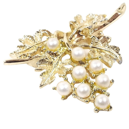 Front view of the retro vintage Emmons faux pearl brooch pin. The metal is gold tone in color and is shaped like a cluster of grapes hanging off a vine. There are round imitation pearls as the grapes.