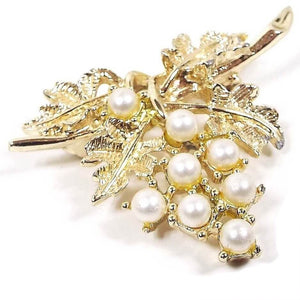 Front view of the retro vintage Emmons faux pearl brooch pin. The metal is gold tone in color and is shaped like a cluster of grapes hanging off a vine. There are round imitation pearls as the grapes.