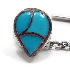 Enlarged view of the 1970's retro vintage faux turquoise tie tack. The metal is darkened silver tone in color and is teardrop in shape. There are three areas of inlaid blue glass imitation turquoise. 