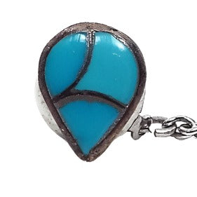 Enlarged view of the 1970's retro vintage faux turquoise tie tack. The metal is darkened silver tone in color and is teardrop in shape. There are three areas of inlaid blue glass imitation turquoise. 