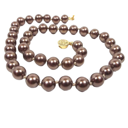 Front view of the Mid Century vintage brown faux pearl necklace. There is a single strand of chocolate brown coated glass round beads. The beads are hand knotted in between each one and there is a gold tone filigree box clasp at the end.