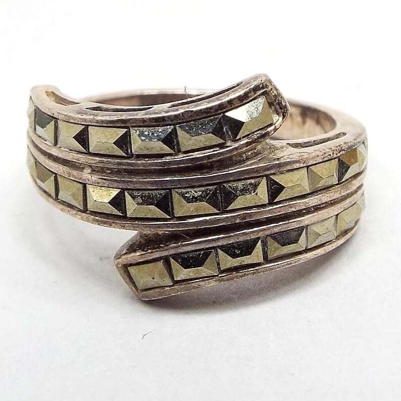 Front view of the retro vintage sterling silver hematite bypass ring. It has three curled around sections that bypass at the top. The sterling is darkened from age. The hematite stones are baguette style and are channel set.