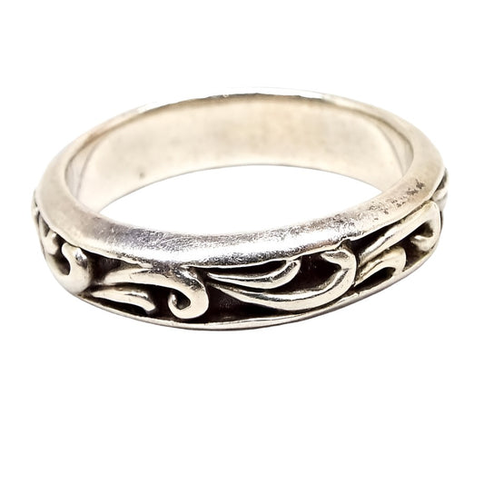 Side view of the outer edge of the retro vintage sterling silver leaf band. The sterling is slightly darkened. The outer edge has a curled leaf like design all the way around the band. The recesses of the design are dark gray in color for an antiqued look. There are some darkened lines on the inside of the band from age.