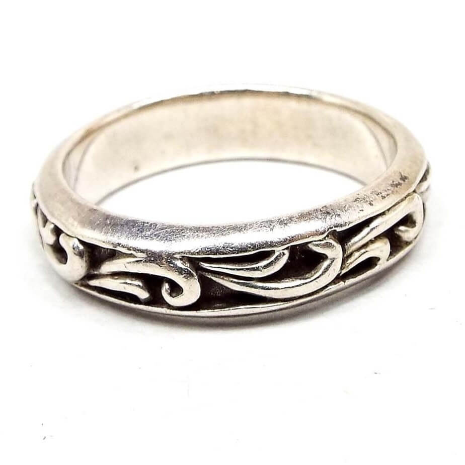 Side view of the outer edge of the retro vintage sterling silver leaf band. The sterling is slightly darkened. The outer edge has a curled leaf like design all the way around the band. The recesses of the design are dark gray in color for an antiqued look. There are some darkened lines on the inside of the band from age.