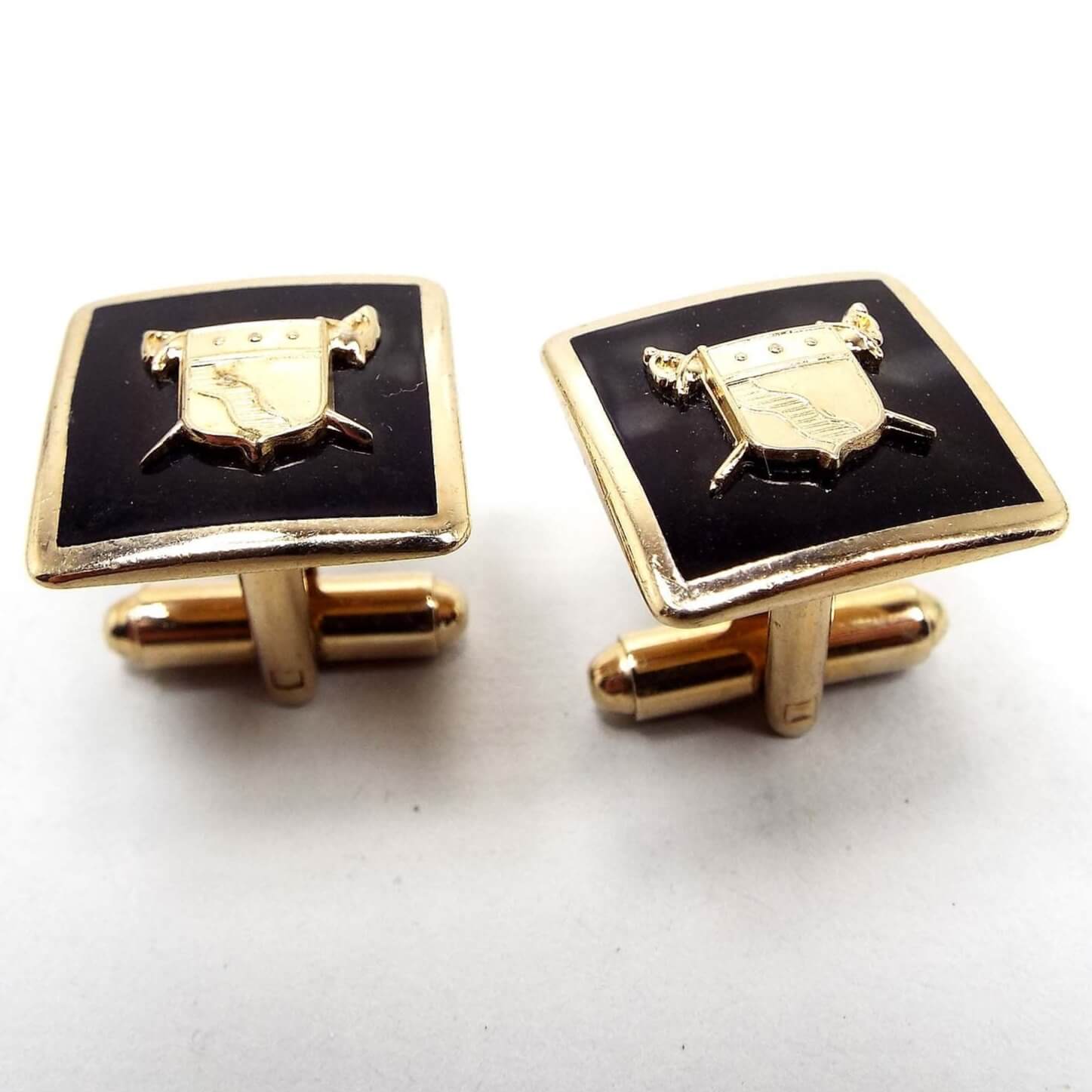 Top view of the Mid Century vintage Coat of Arms cufflinks. The metal is gold tone in color. The fronts have black enamel with a gold tone metal shield with swords design. 