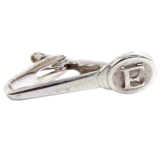Front view of the Mid Century vintage Shields initial tie clip. It is silver tone in color. The end is round and textured and has the letter E on it.
