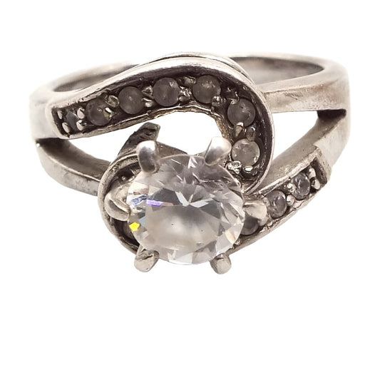 Front view of the retro vintage cubic zirconia cocktail ring. The sterling silver is slightly darkened from age. The band is split style at the top and half of each side has a row of small prong set CZ stones that is curved around the larger CZ middle stone. 