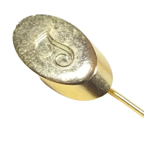 Enlarged view of the top of the Mid Century vintage initial stick pin. The metal is gold tone in color. There is an oval shape at the top with fancy script letter T engraved on it.