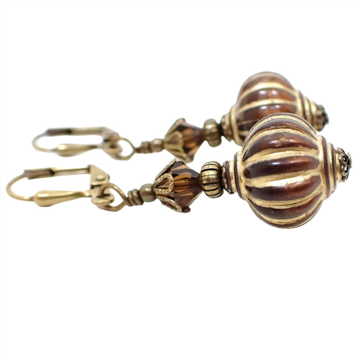Side view of the handmade lantern drop earrings. The metal is antiqued brass in color. There are dark brown faceted glass crystal beads at the top and brown acrylic lantern shape beads at the bottom. The bottom beads have antiqued gold stripes painted on them.