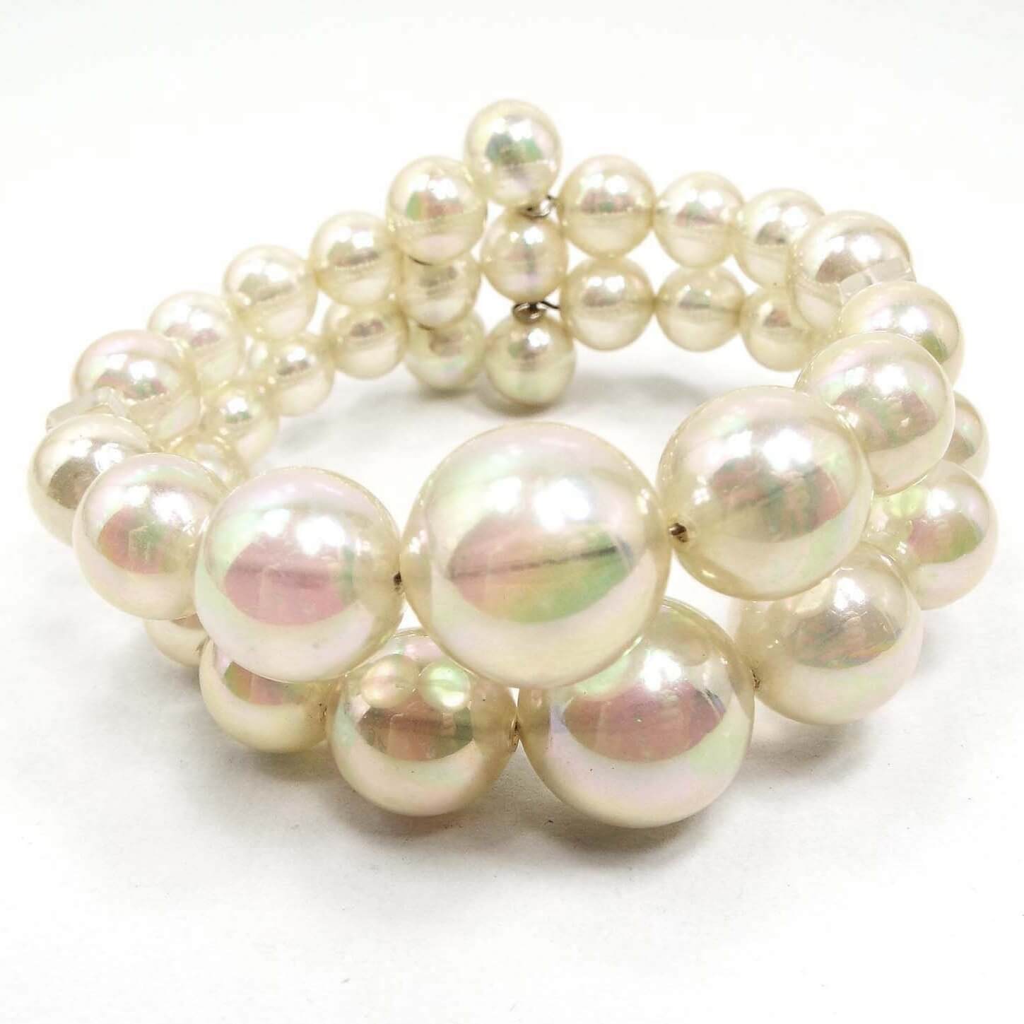Front view of the Mid Century vintage AB plastic beaded memory wire bracelet. It has pearly aurora borealis semi translucent white round beads in two rows around the bracelet. The memory wire can be seen inside and between the beads.